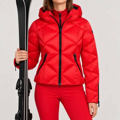 Goldbergh women's Harumi Ski Jacket in Flame Red – model ski pose standing with skis, plain cuffs without fur. AI-generated from manufacturer imagery.
