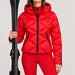 Goldbergh women's Harumi Ski Jacket in Flame Red – model ski pose standing with skis, plain cuffs without fur. AI-generated from manufacturer imagery.